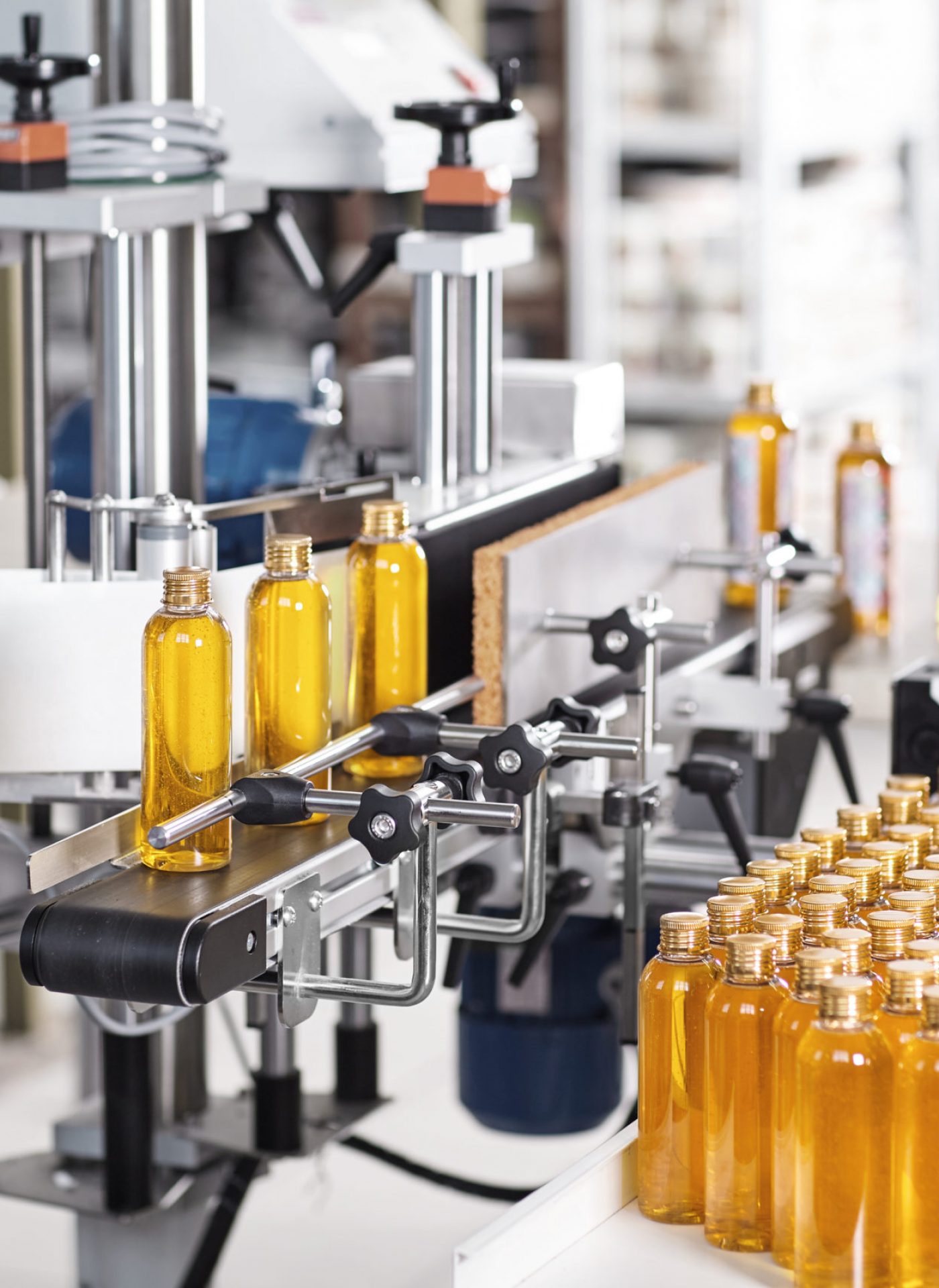 Horizontal shot of cosmetics or pharmacy plant with automated equipment. Transparent plastic bottles filled with yellow substance standing on desk and conveyor line, ready for transportation